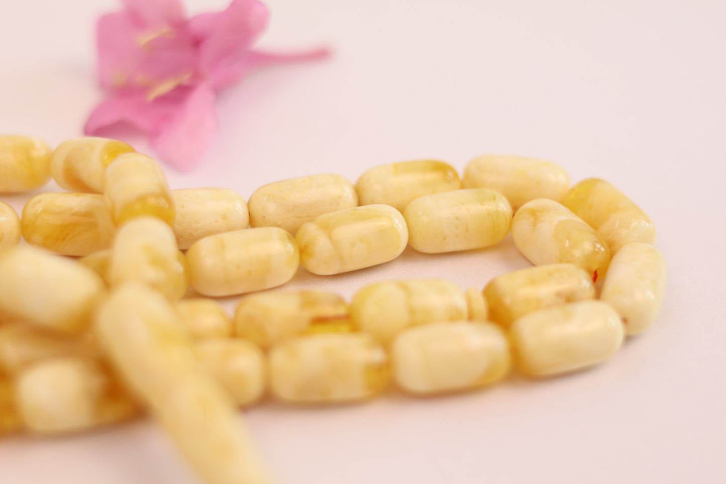 Close-up of a string of yellow beads on a light pink background with a pink flower.