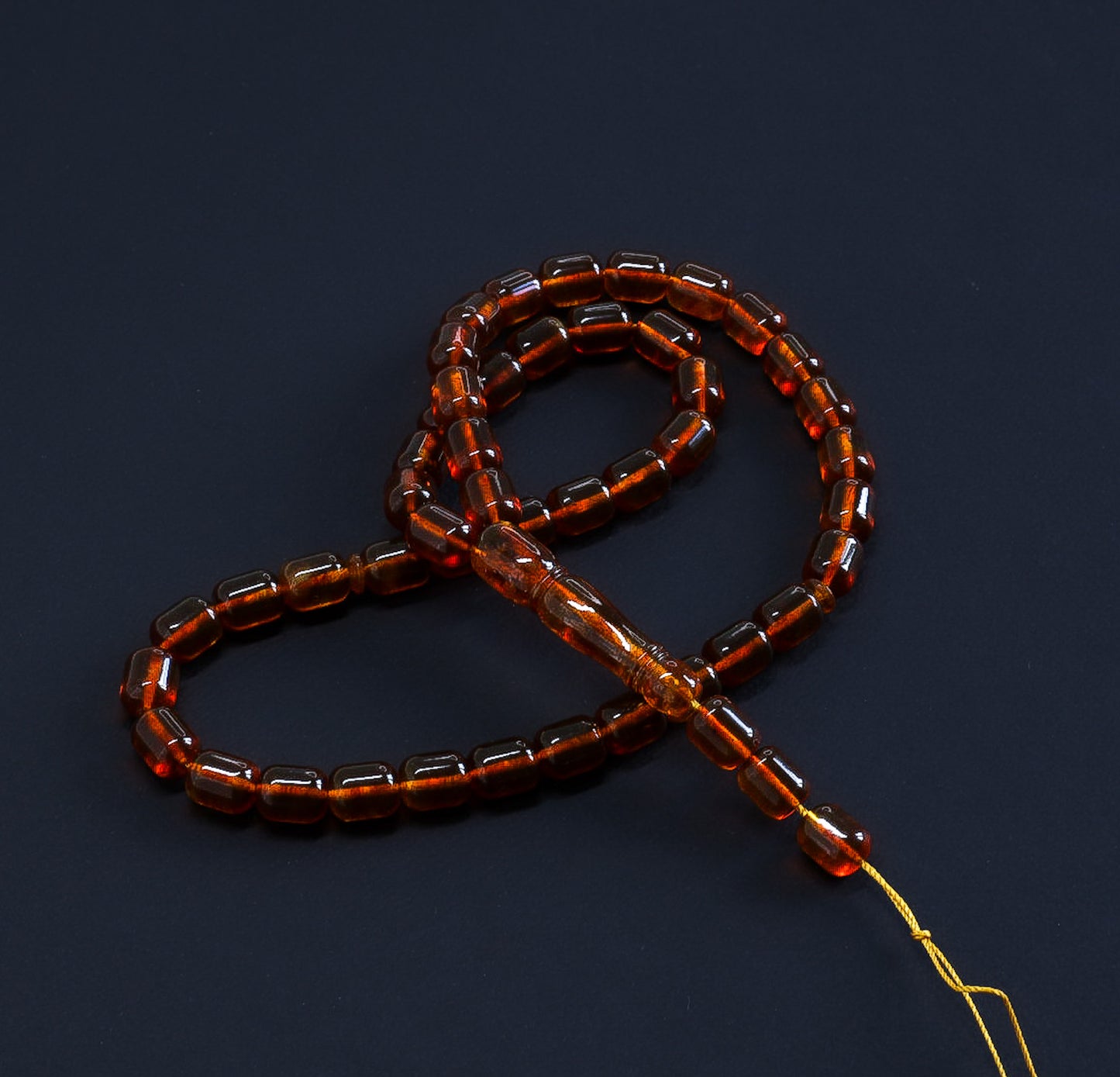 Top-down view of the transparent amber Tasbih (تسبيح كهرمان), highlighting the rich cherry brown color.
