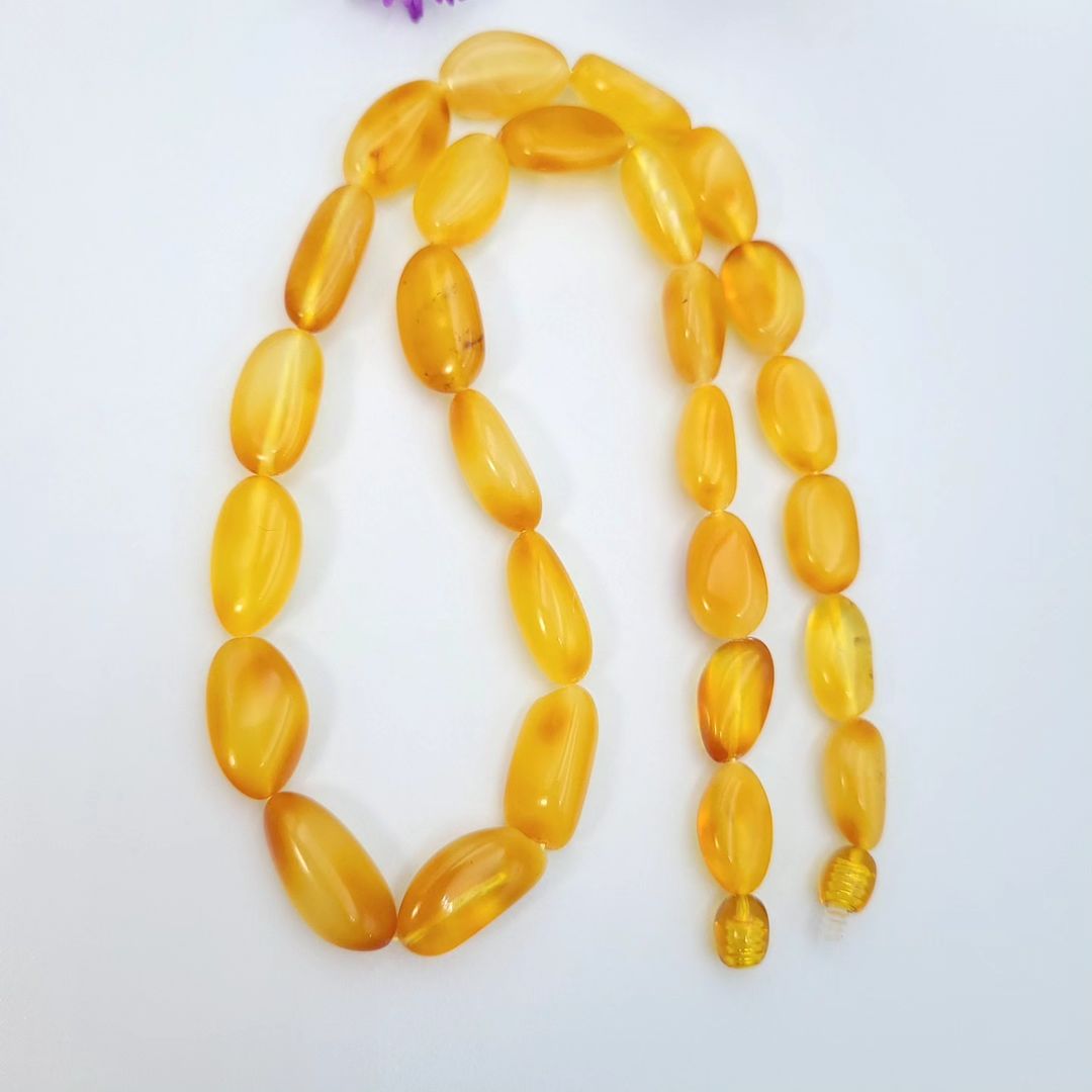 A view of a bright honey-yellow amber necklace hanging in a loose, inverted U-shape on a white background. The polished, tumbled, irregular beads are graduated. The necklace ends are visible at the bottom right.