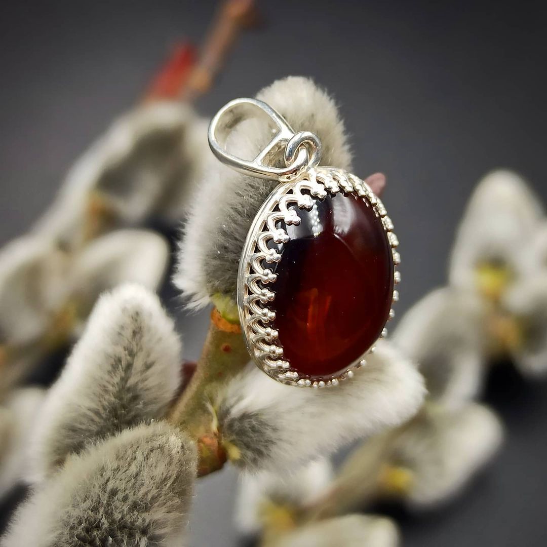 A mahogany amber pendant with a silver frame displayed on a floral stem.