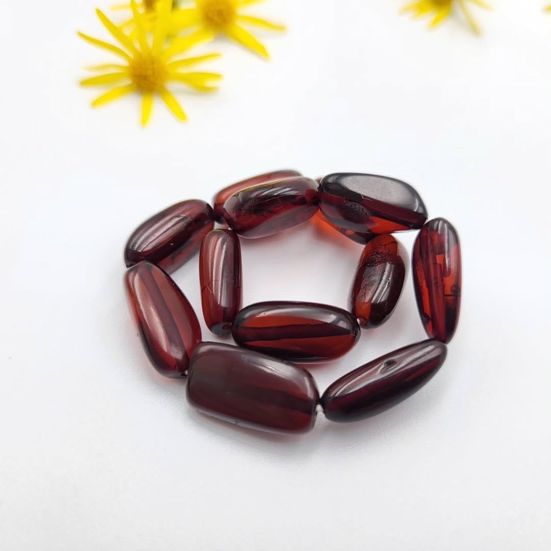 Dunkel Kirsch Bernstein Armband, präsentiert mit natürlicher Dekoration
auf weißem Hintergrund.