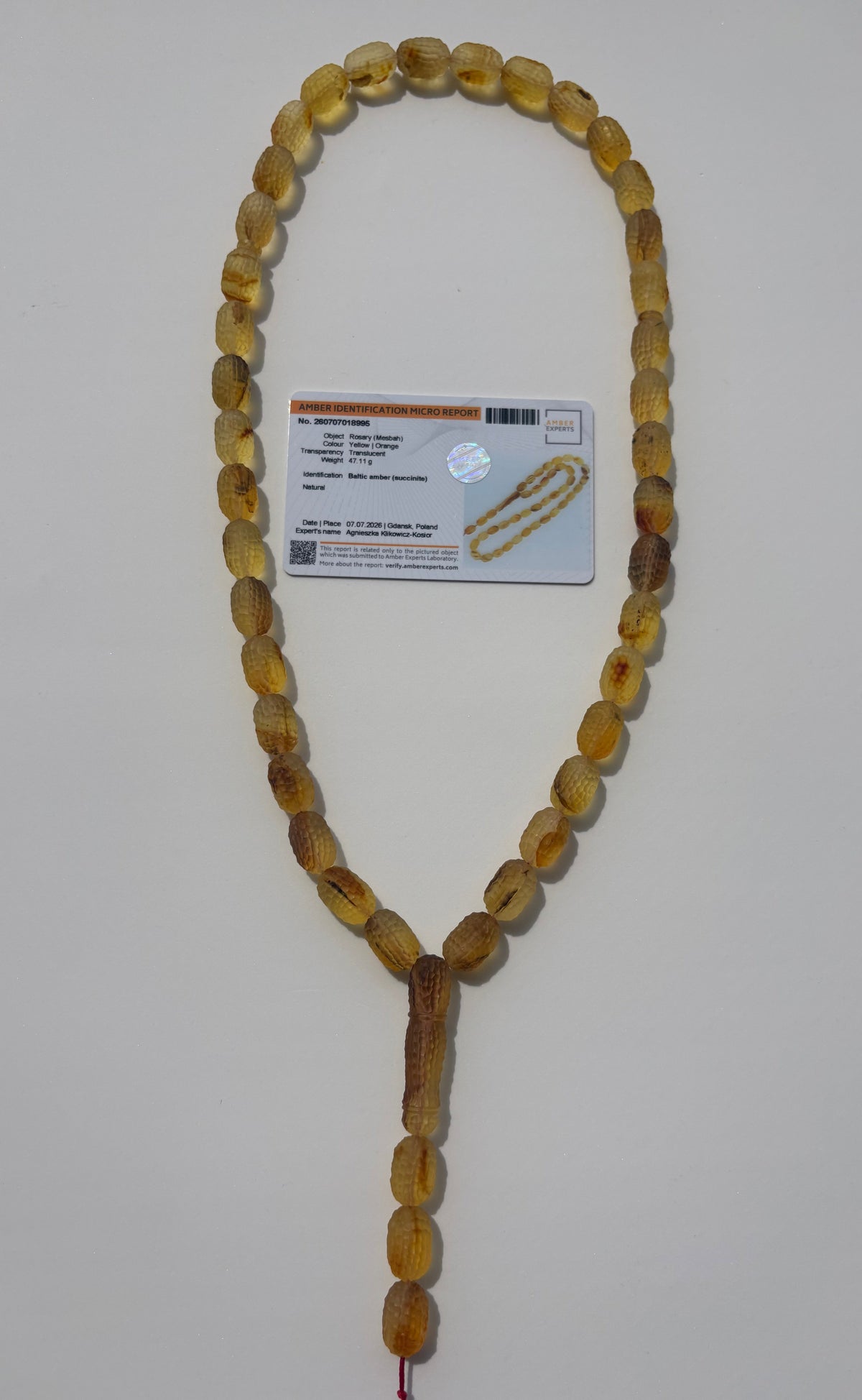 A strand of oval amber prayer beads with a tassel, laid out on a light gray background next to a product card.
