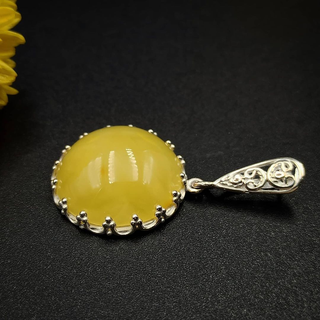 Seitenansicht des Milchgelben Bernstein-Anhängers mit ornamentaler Silberöse und Zierfassung.
