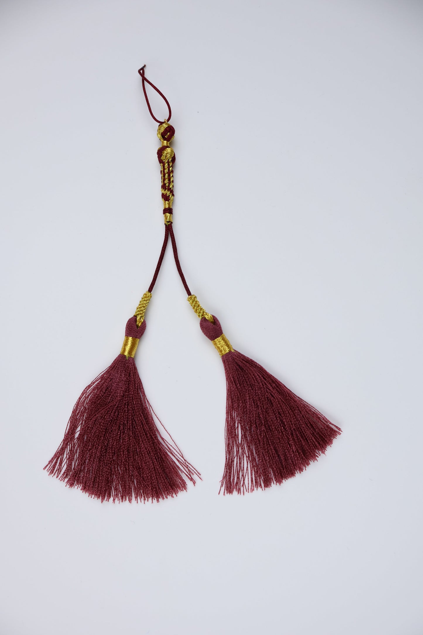 A pair of traditional arabic tassels made of deep burgundy red silk with gold metallic accents and a decorative knot, displayed on a clean white background.