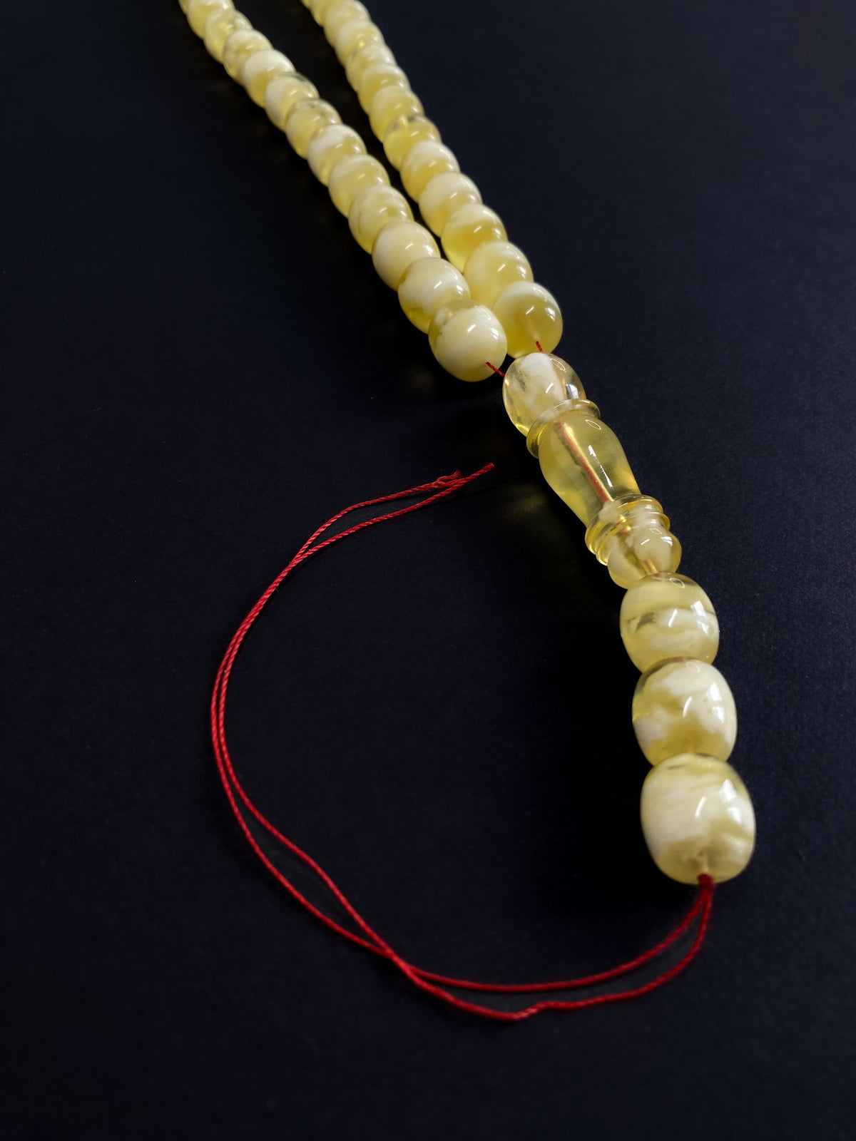 Detailed shot of the سبحة فاخرة (luxury rosary) tassel and the signature 'Imam' bead, made of genuine Baltic amber.
