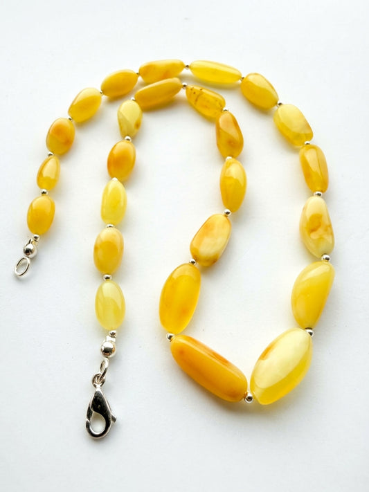 17.8g butterscotch lemon yellow Baltic amber bead necklace with silver spacers and clasp resting on a white background near a flower.