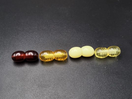 Vier Kunststoff-Sicherheits-Schraubverschlüsse für Bernsteinketten in verschiedenen Farben: Dunkelbraun, Honig, Hellgelb und Transparent.