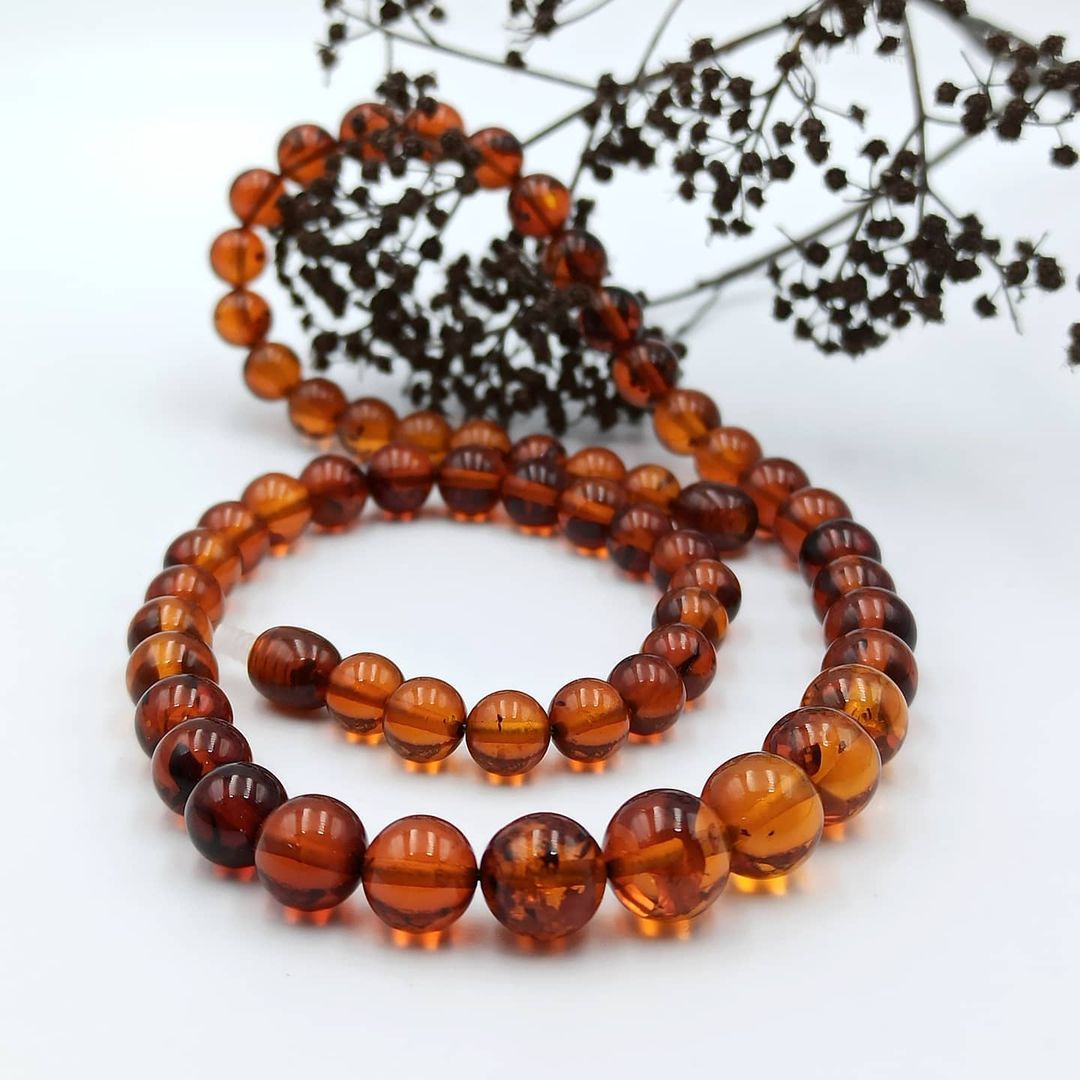 A Tetibel amber necklace with reddish-brown beads of varying sizes, displayed against a white background with some dried plant leaves.
