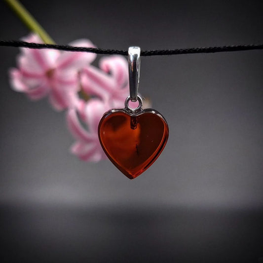 A heart-shaped amber pendant with silver detailing, displayed against a floral background.