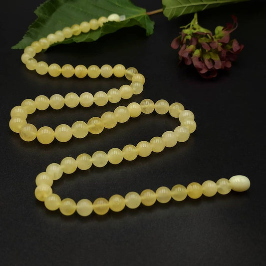 A yellow amber necklace with round beads laid out on a dark background, alongside a leaf and a berry.