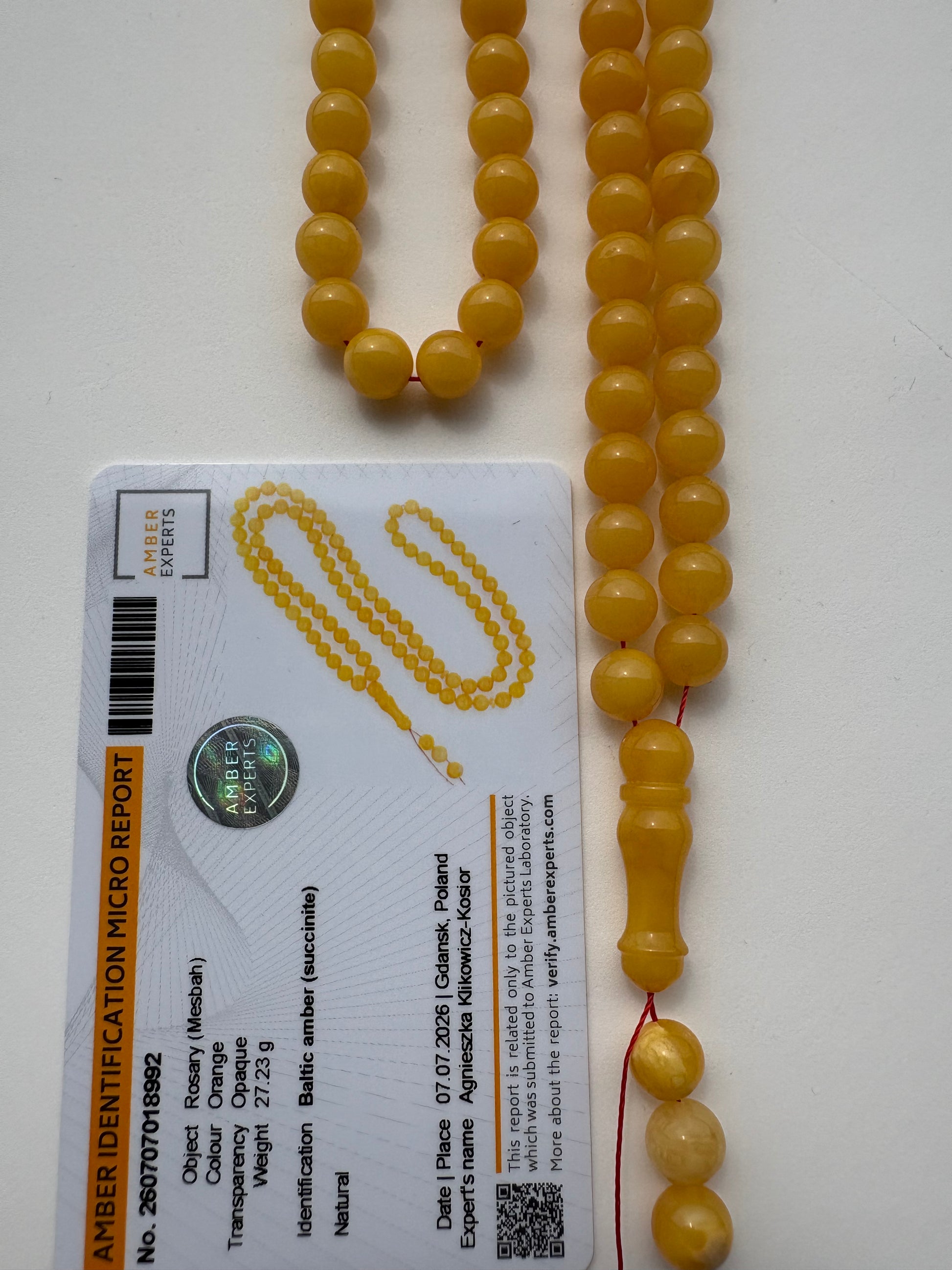 A strand of round yellow amber beads laid out next to an amber identification micro report card on a white background.