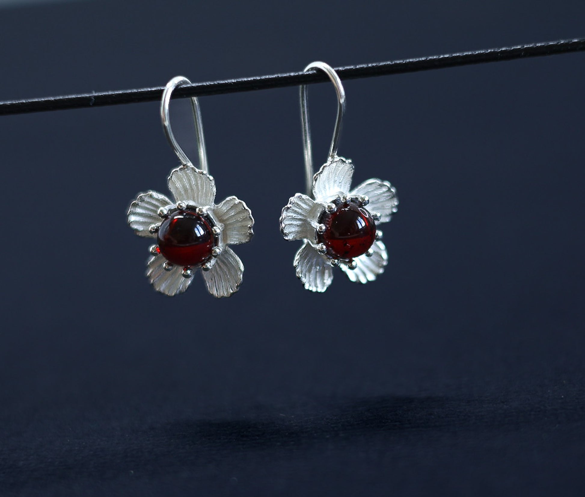 Ohrringe im Antik-Stil mit Silberblume und Kirschbernstein, präsentiert mit dem Ohrhaken vor hellem Hintergrund.