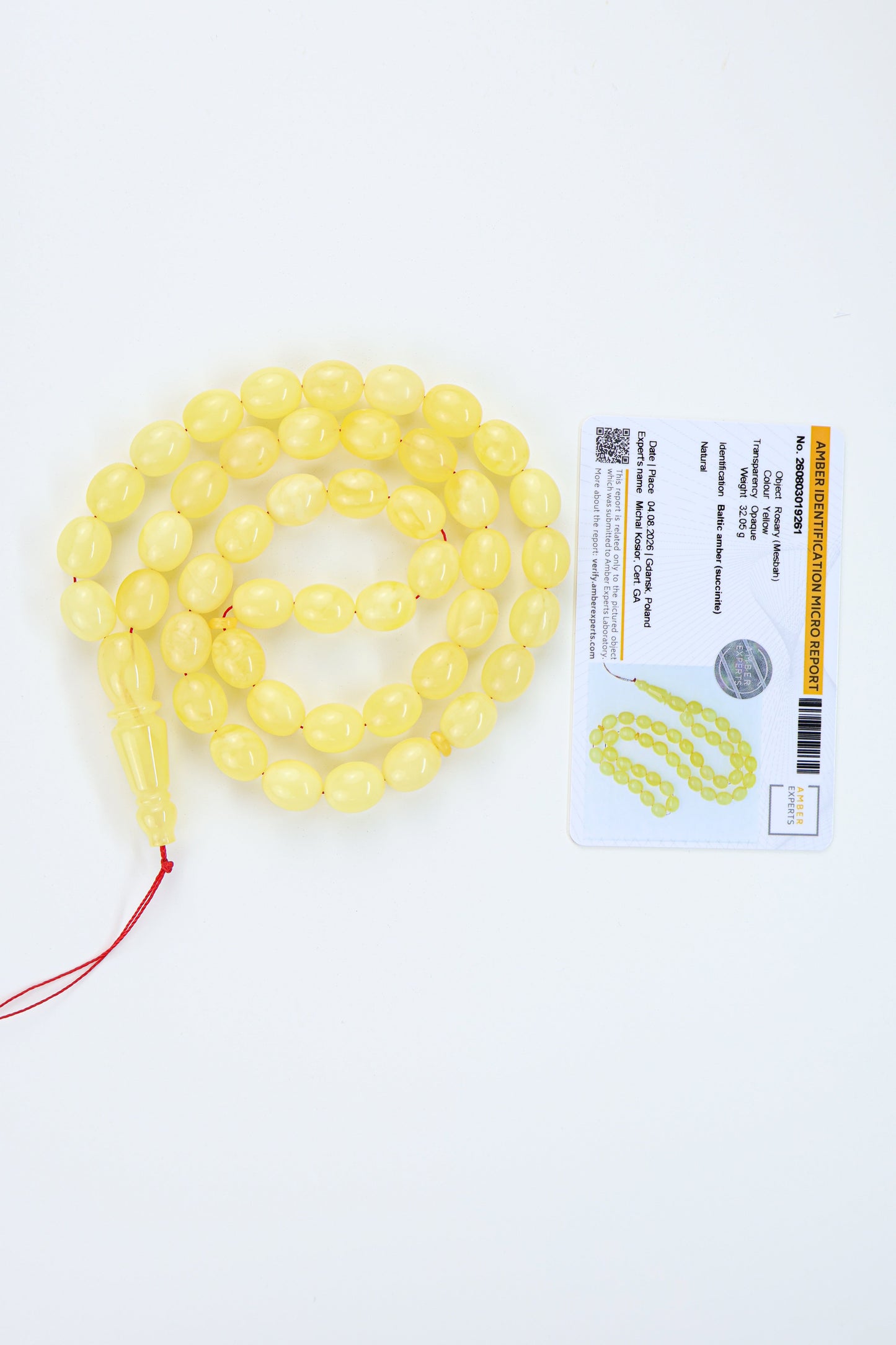 Yellow amber  translucent prayer beads with a red cord and tassel, displayed next to a labolatory certificate card on a white background.