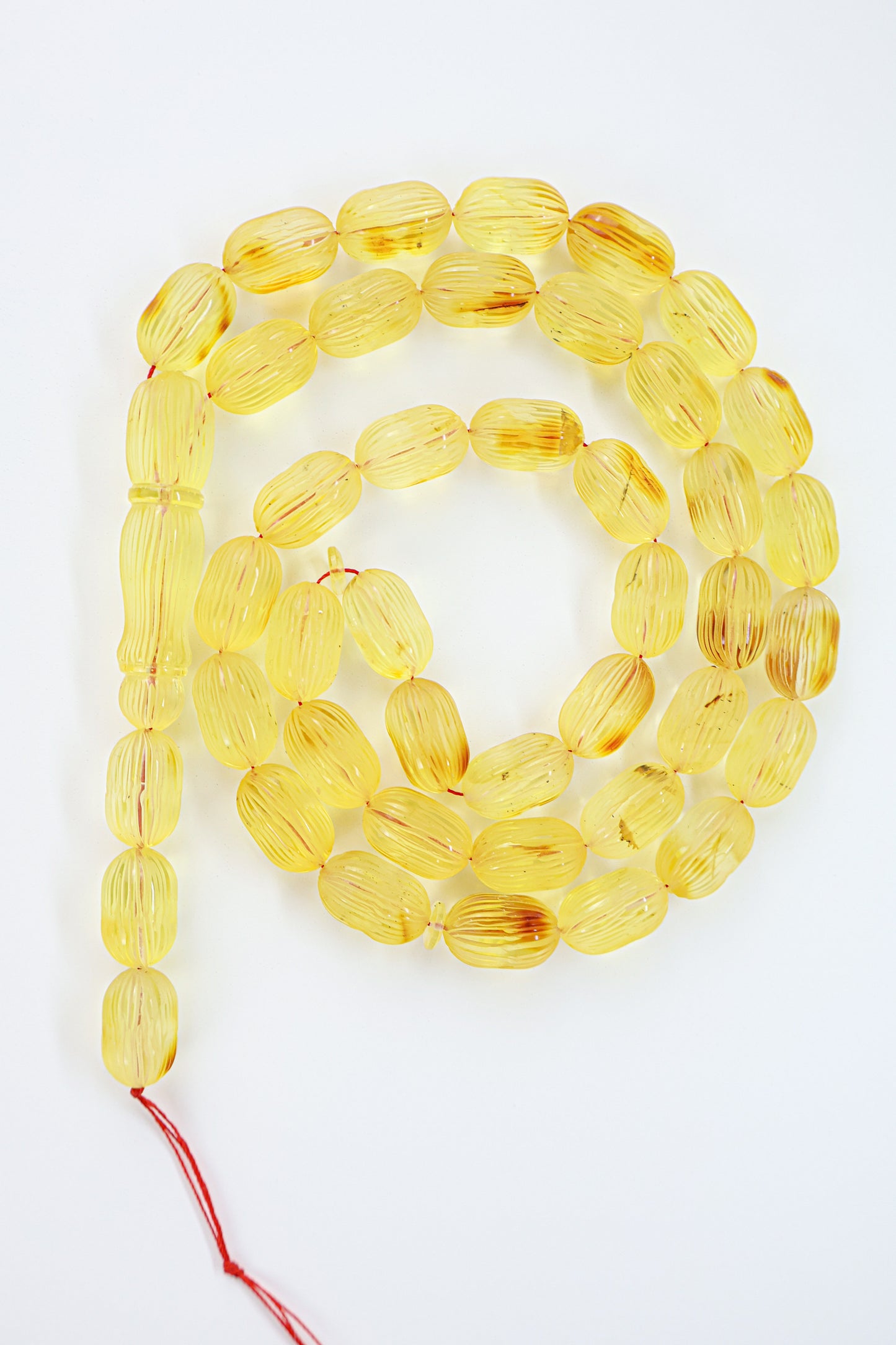 Authentic grooved hand-carved yellow-brown Baltic amber misbaha strand displaying natural minor imperfections and a matching carved amber imam.