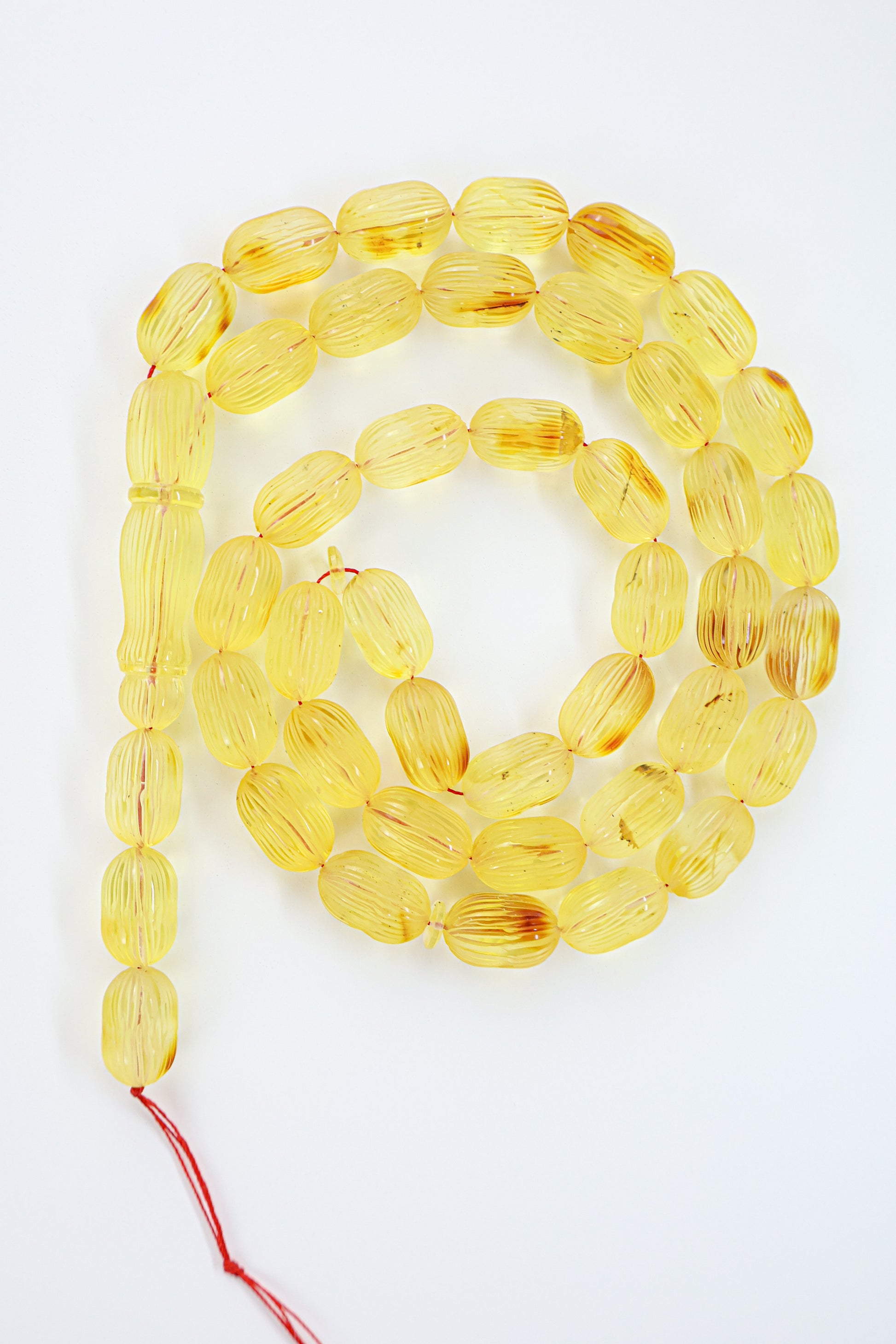 Authentic grooved hand-carved yellow-brown Baltic amber misbaha strand displaying natural minor imperfections and a matching carved amber imam.
