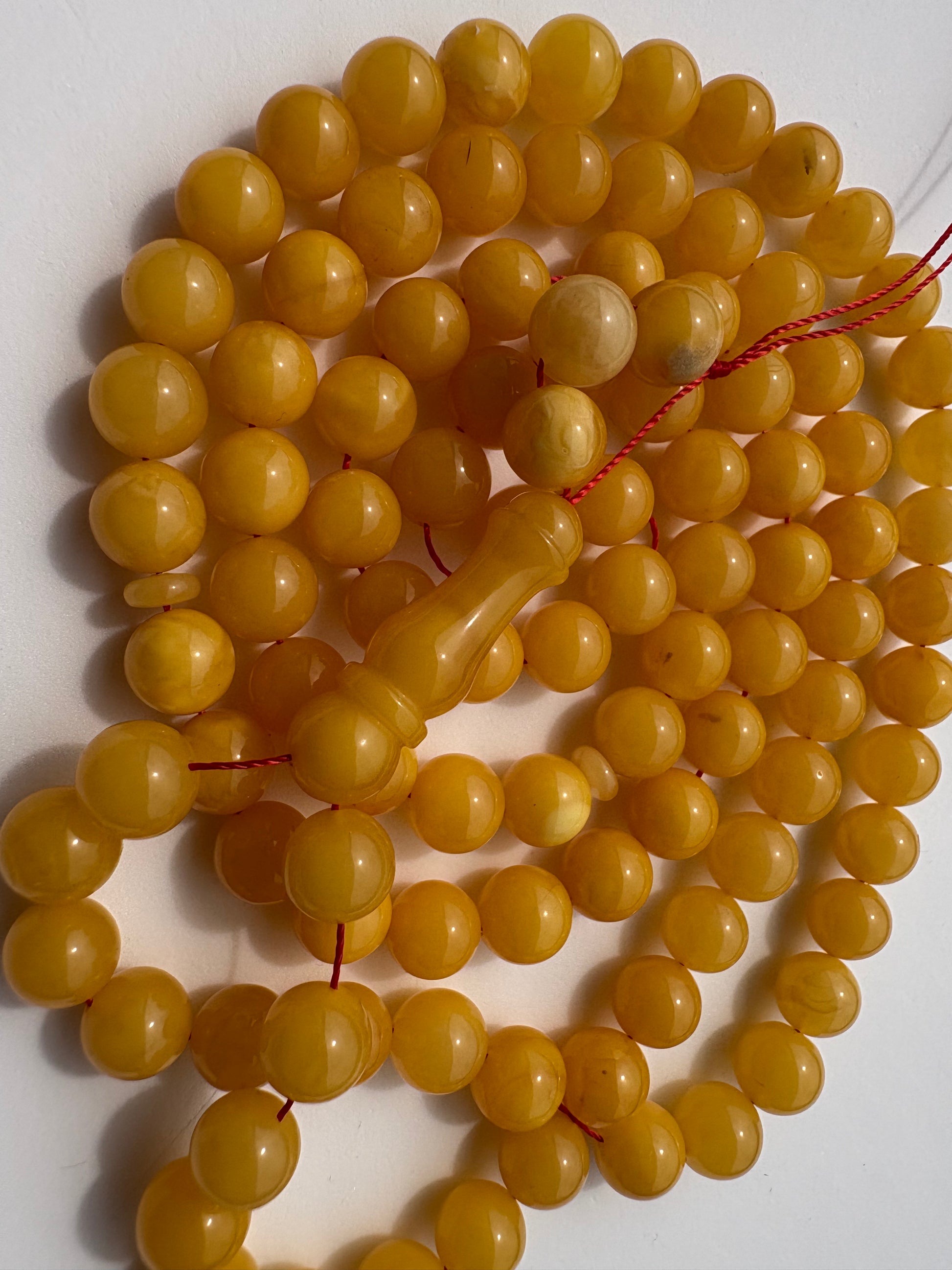 A strand of round yellow-gold beads strung on a red cord, with a matching cylindrical bead separator, photographed on a plain white background.