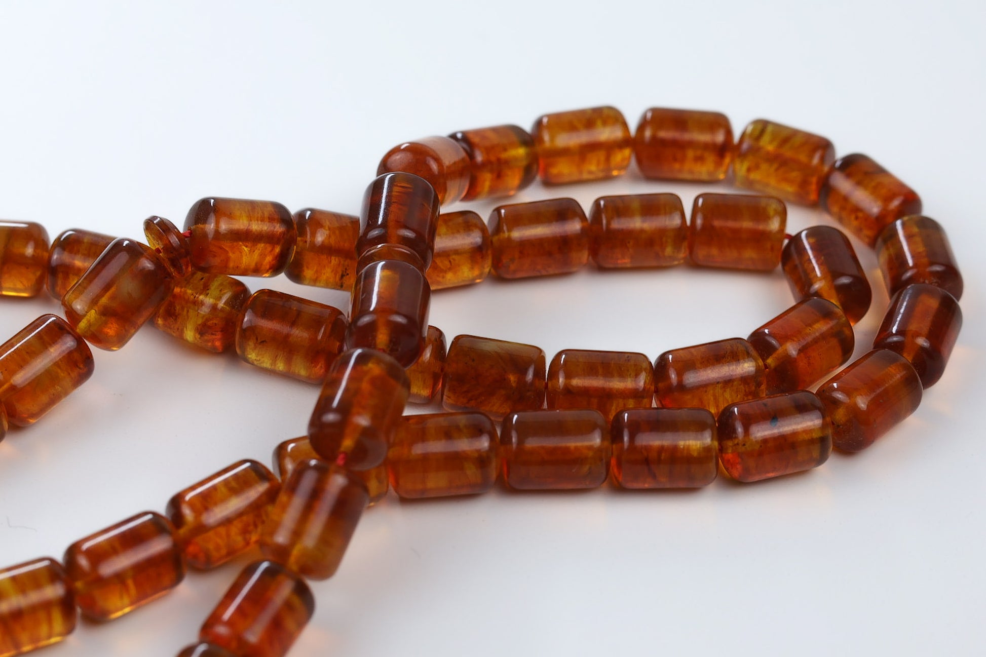 Close-up of cognac pressed Baltic amber rosary beads in barrel shape, translucent honey amber texture