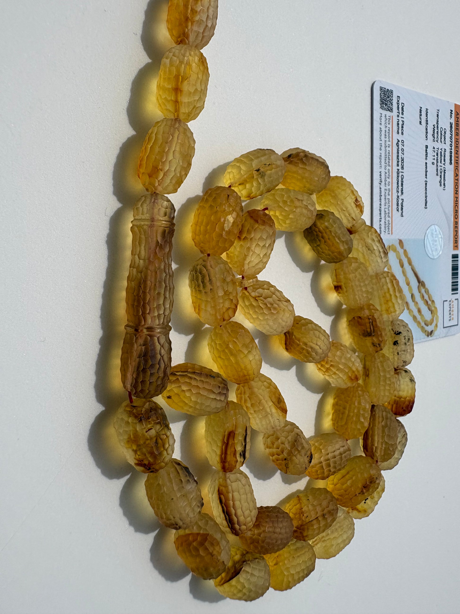A strand of carved amber beads with a textured, ribbed surface, coiled on a white surface next to a product information card.