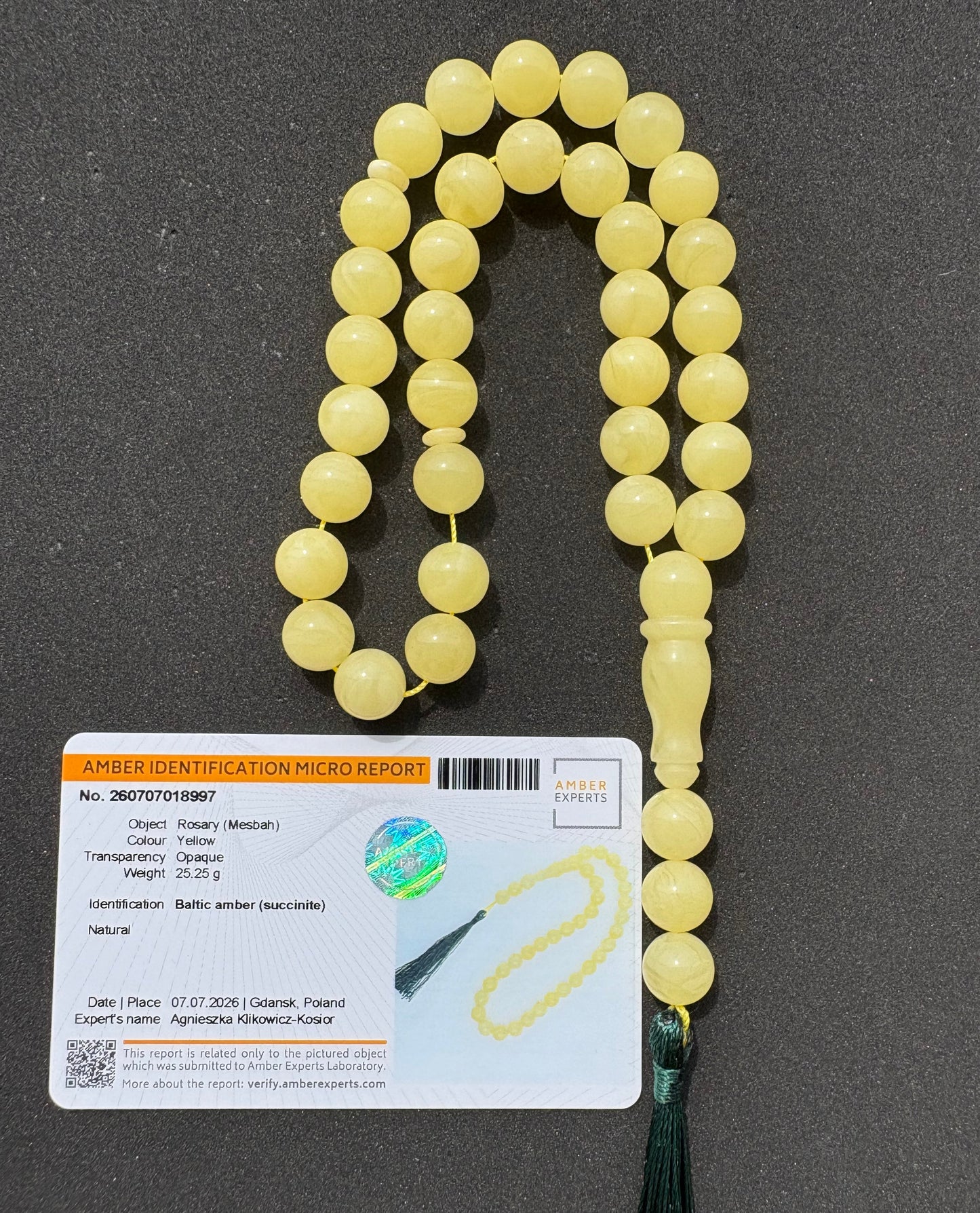 Tetibel yellow Islamic prayer beads (Tasbih) with a dark green tassel, displayed next to a product information card on a dark gray background.