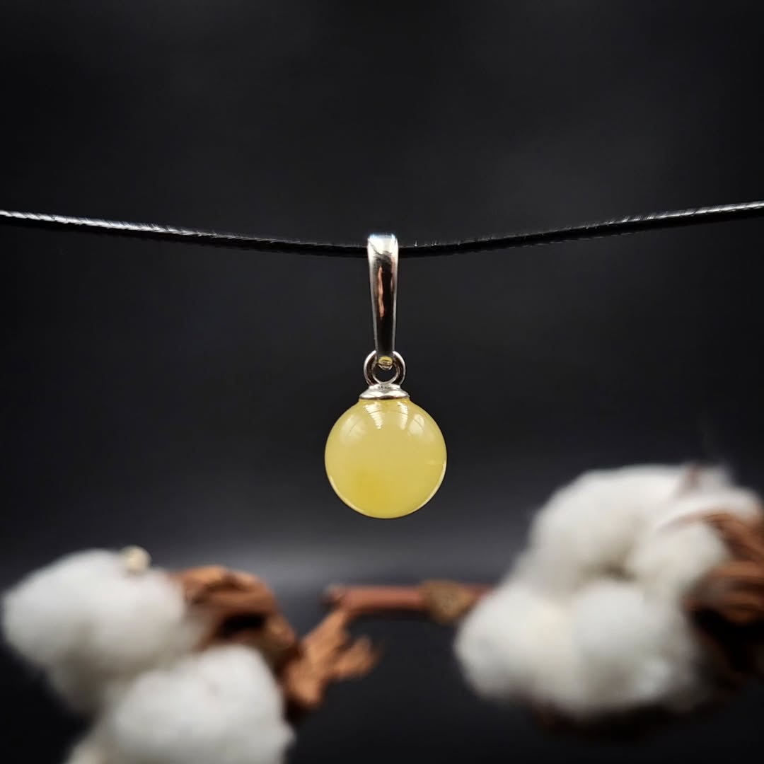 Bernstein Kugel Silber Anhänger milchig, minimalistisch, auf schwarzem Grund.