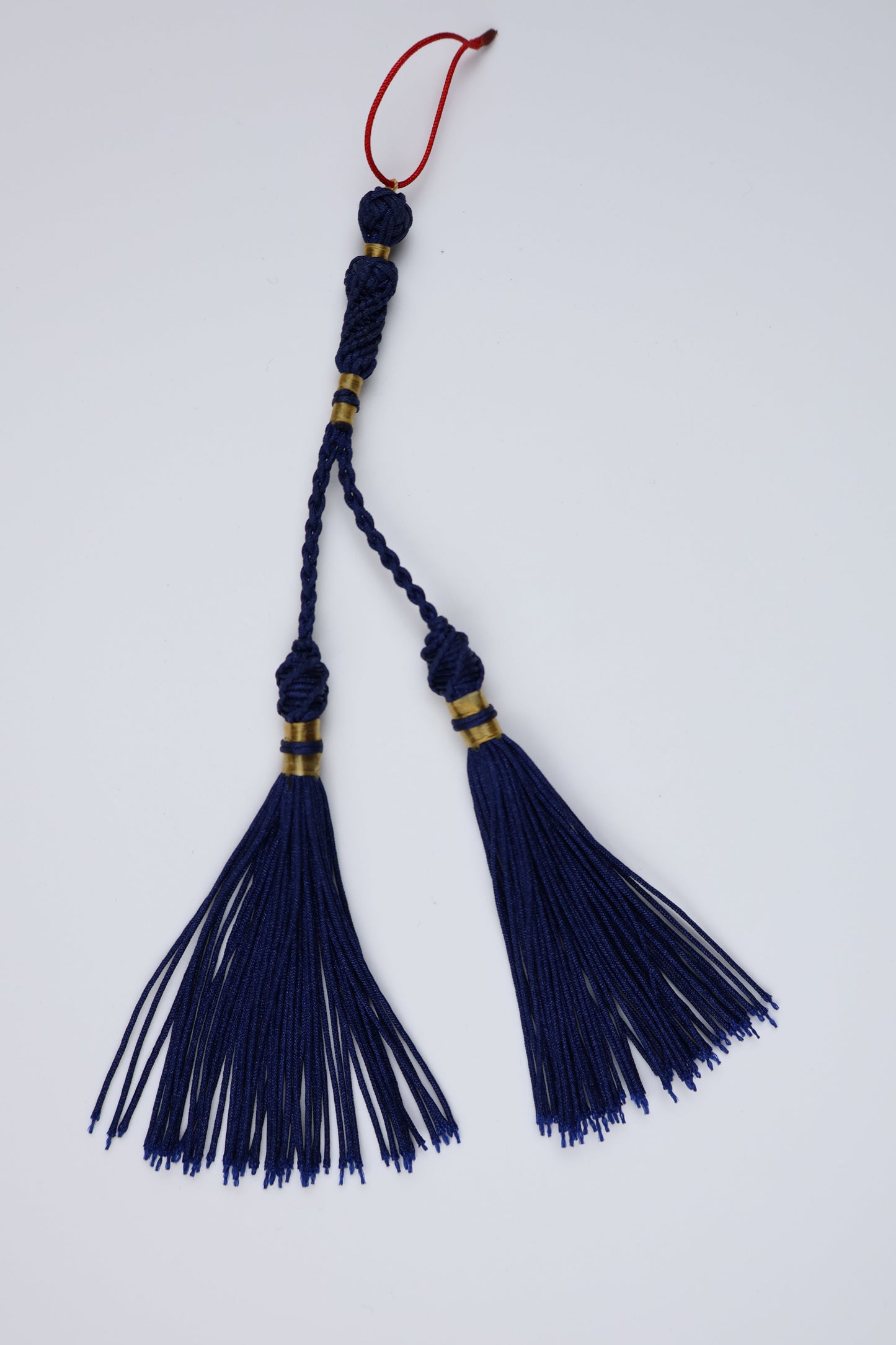 A traditional Arabic silk tassel ornament, mesbah accesoire, featuring two large navy blue tassels, a braided cord, gold metallic rings, and a small red hanging string on a plain white background.