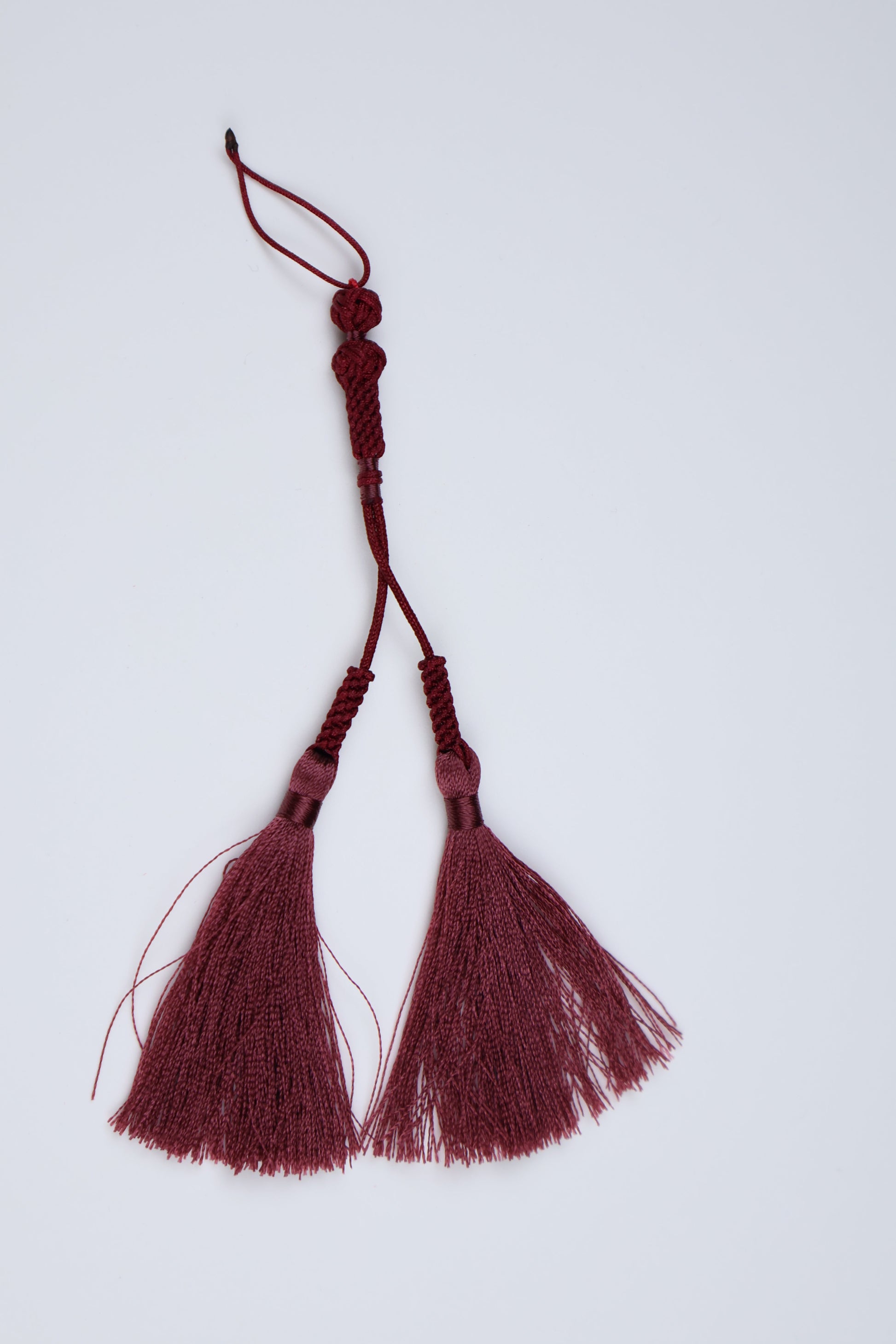 A burgundy tassel ornaments with knotted cords and decorative beads, perfect for prayer beads
