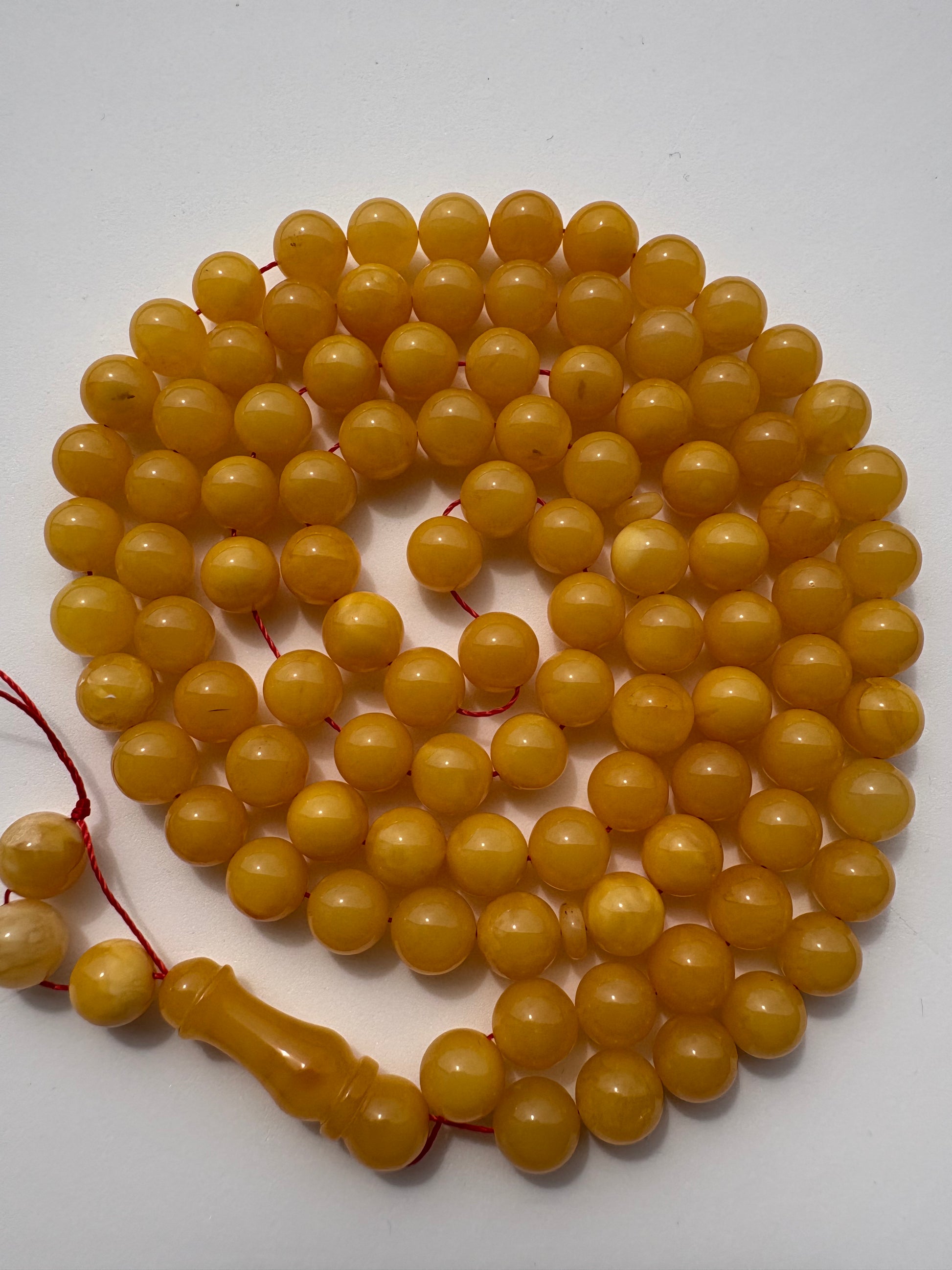 A strand of round, polished yellow-gold beads on a red cord, coiled on a plain white surface.