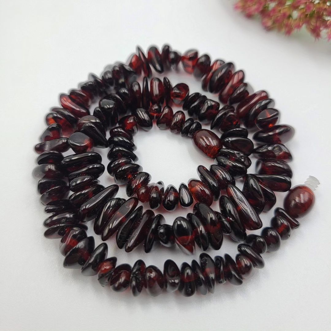 Nahaufnahme der kirschroten, unpolierten Bernstein Nuggets, dunkel und glänzend, mit rotem Deko-Element.