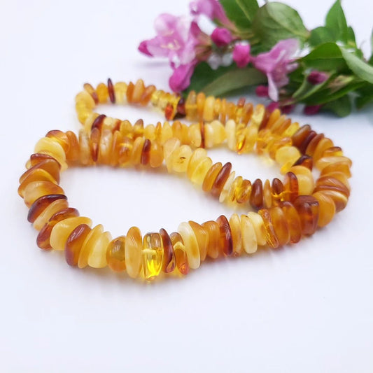 Close-up of a Tetibel genuine Baltic amber nugget necklace, displaying individual raw amber pieces in varied earthy shades with a soft floral accent.