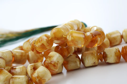 Close-up of pressed amber rosary cube beads showing glossy honey and cognac marbled texture.