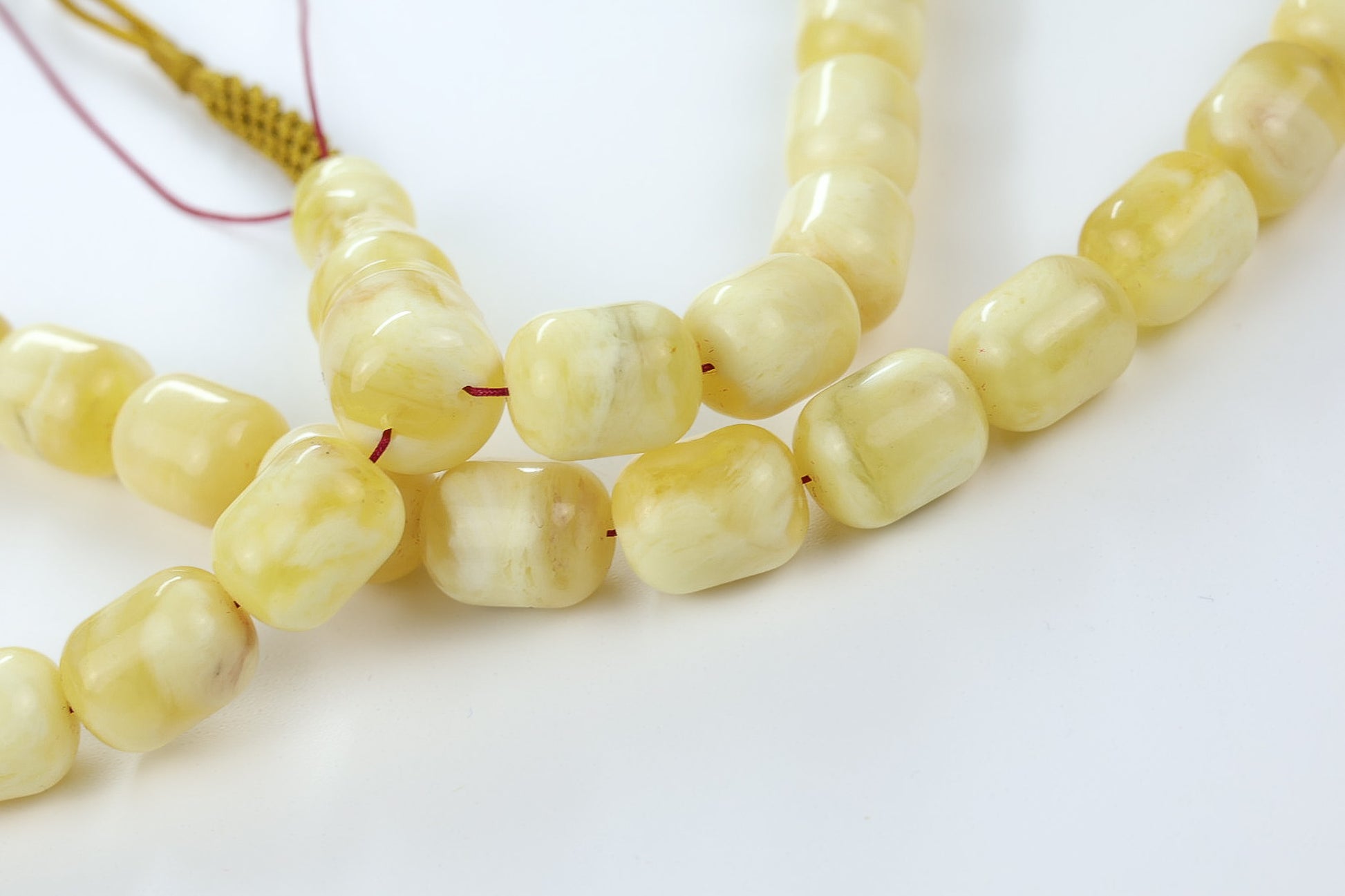 Close-up of light yellow pressed amber rosary beads showing milky texture and polish.