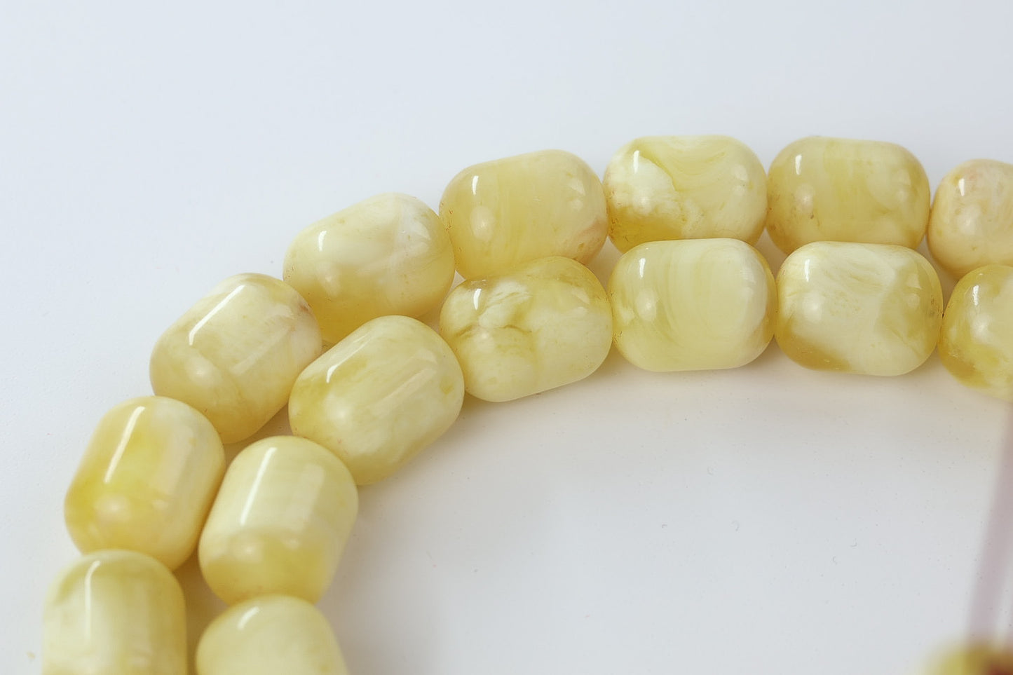 Detail of barrel-shaped imame and gold tassel on light yellow pressed amber rosary.