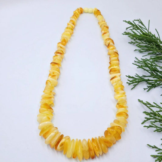 Tetibel Splitterkette aus echtem baltischem Rohbernstein in Butterscotch und Lemon, in Zick-Zack-Form auf weißem Hintergrund mit frischem Grün. Zeigt die ganze Länge und die unpolierten Nugget-Perlen.