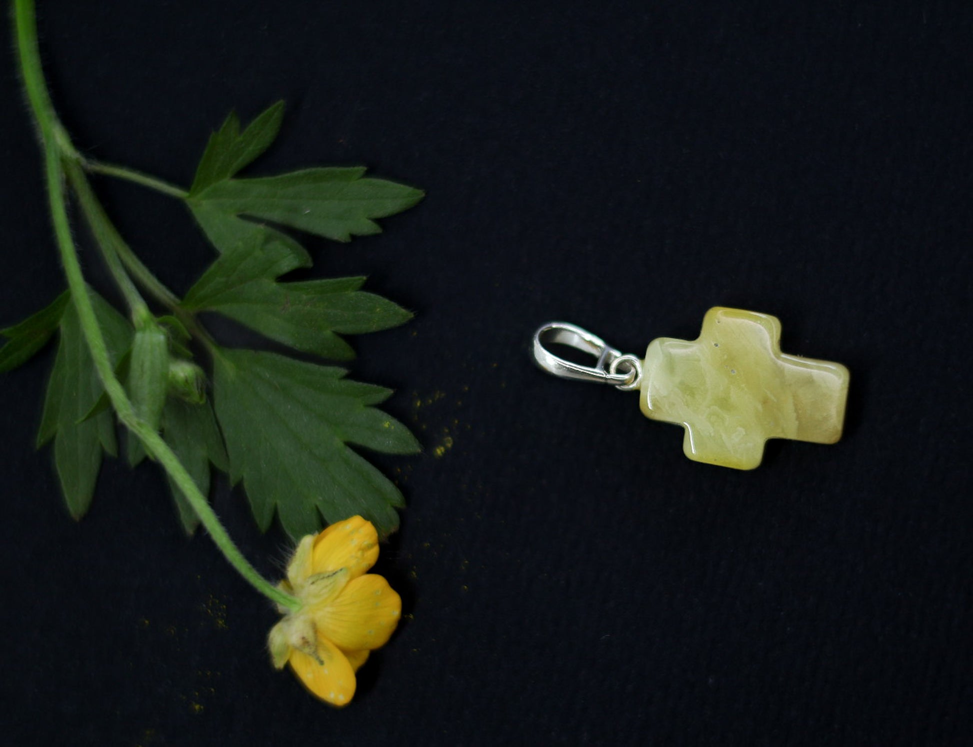 Yellow cross-shaped pendant with green leaf and yellow flower on a dark background.