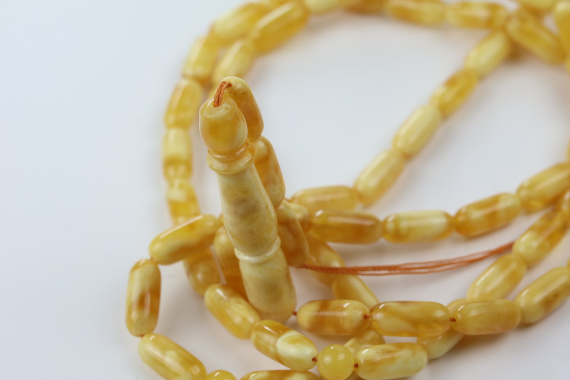 Macro close-up of Tetibel pressed amber oval beads in butterscotch yellow tone, glossy Islamic rosary beads for Europe.