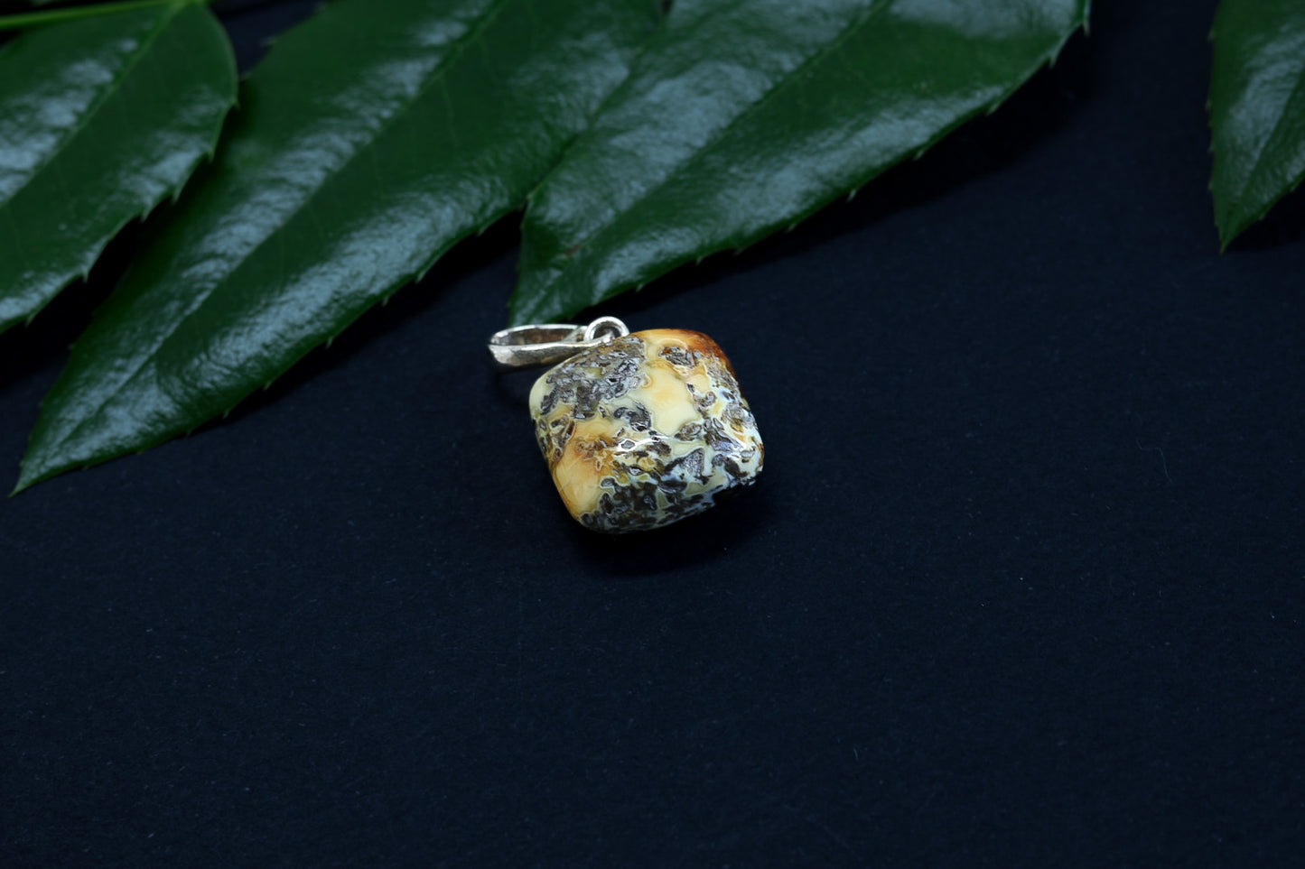 Pendant with textured surface on dark background with green leaves.